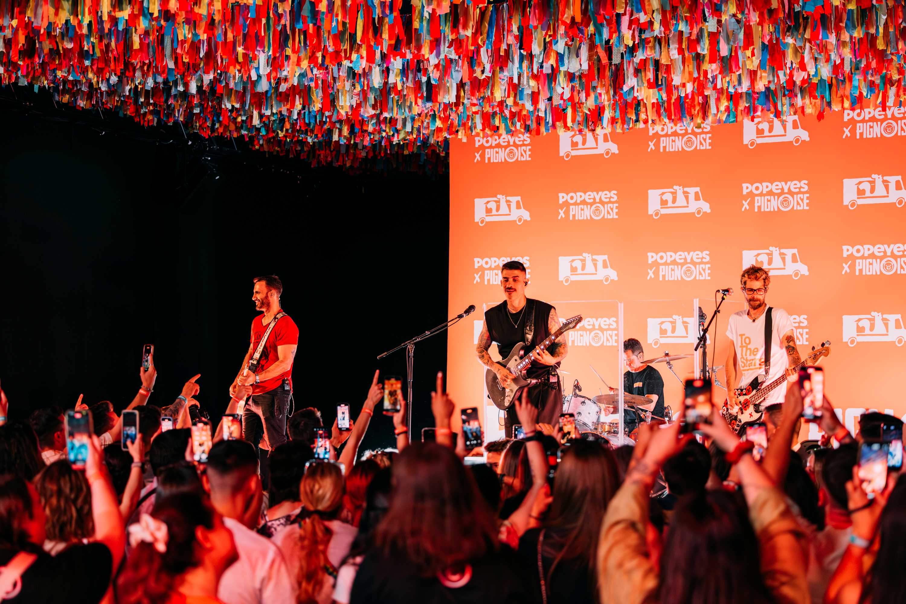 La banda Pignoise tocando un concierto frente a un grupo de personas con los brazos en alto y grabandoles con sus teléfonos